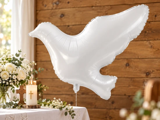 Biały balon gołąb nad stołem udekorowanym kwiatami, świecą z krzyżem i drewnianym krzyżykiem.
