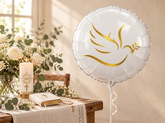 Balon ze złotym gołąbkiem obok stołu ze świecą IHS, książką, różańcem i białymi kwiatami.