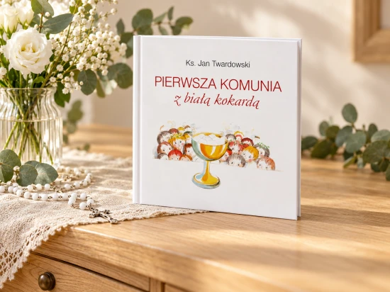 Książka ustawiona pionowo na drewnianej komodzie obok białych kwiatów i różańca.